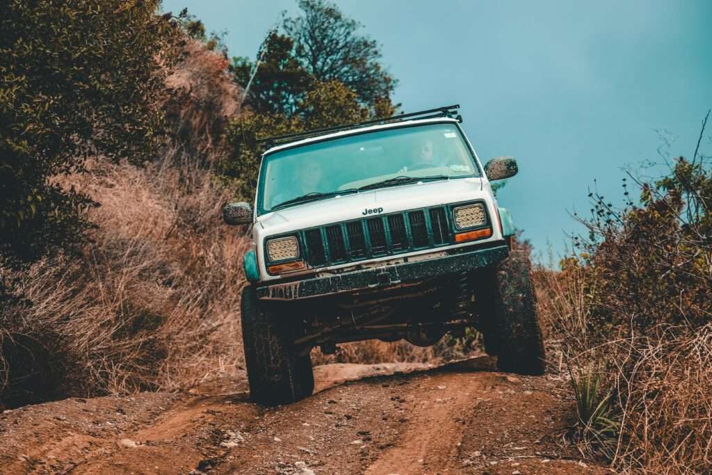 A rugged Jeep navigating a challenging muddy offroad trail through dense forest.
